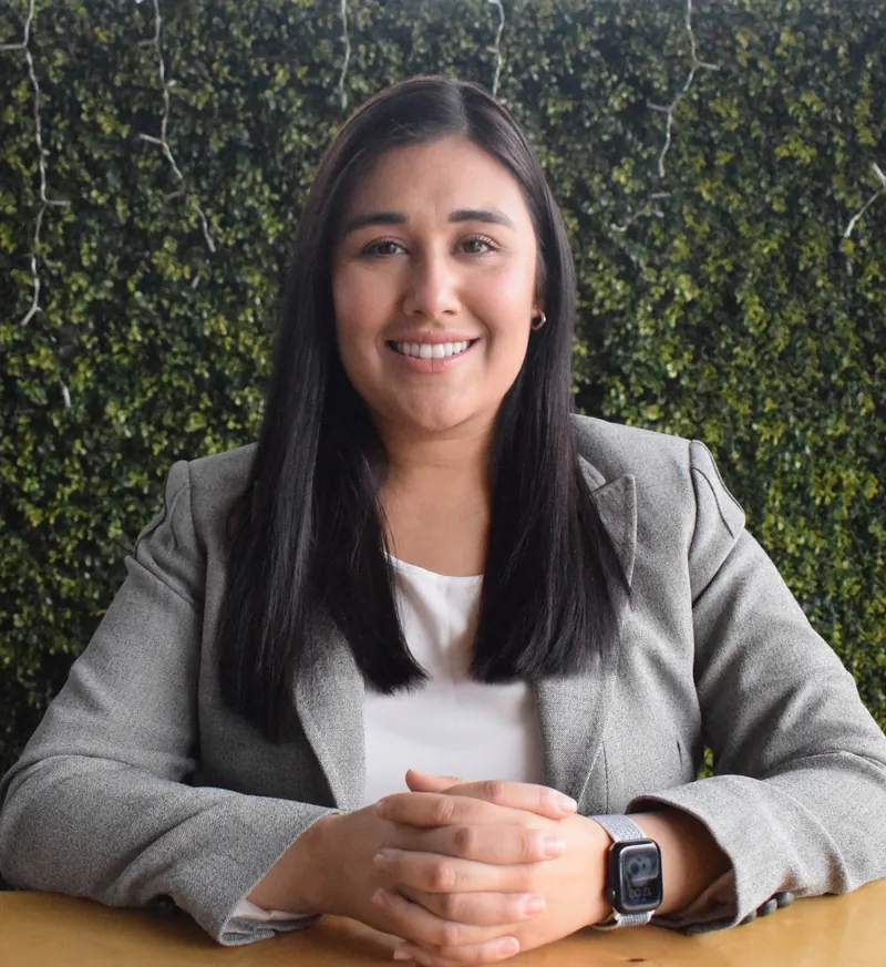 Elizabeth Acuña con blazer gris, sonriendo con las manos entrelazadas